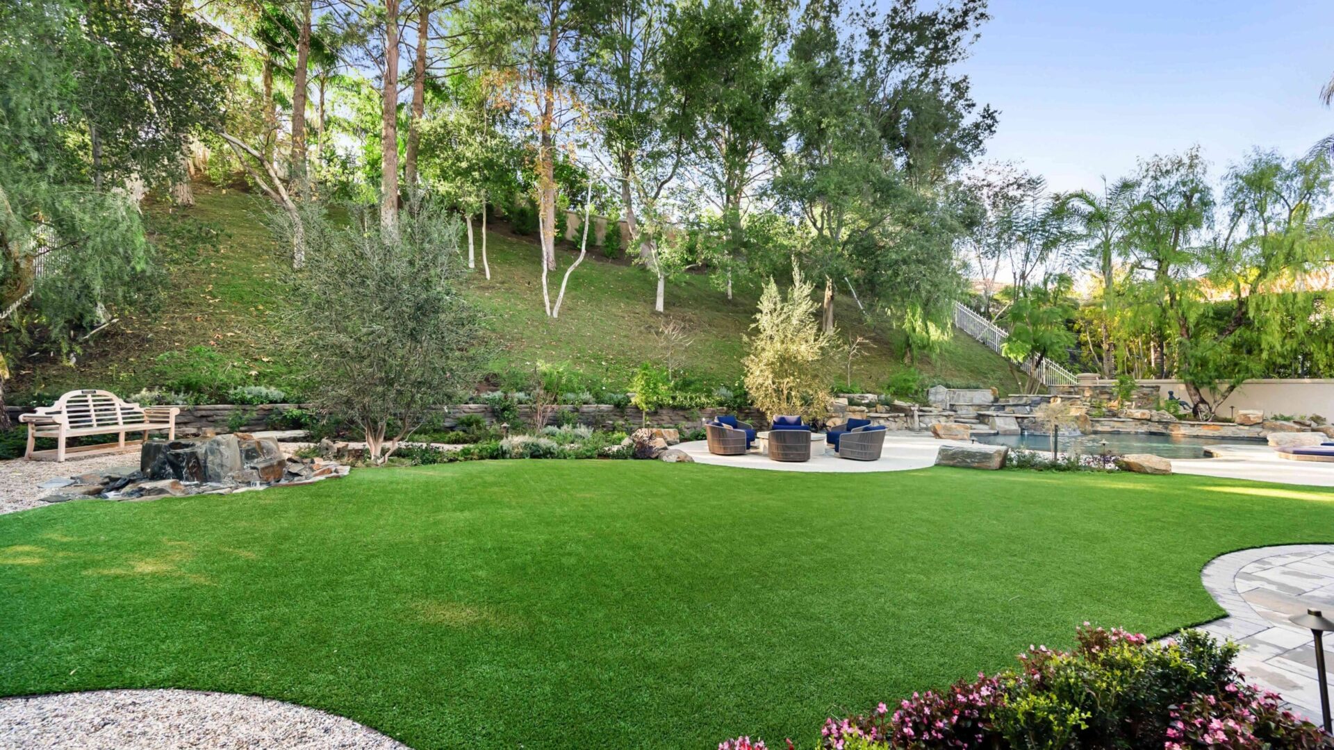 Lush green backyard lawn with landscaping, flowers, trees, and patio seating area