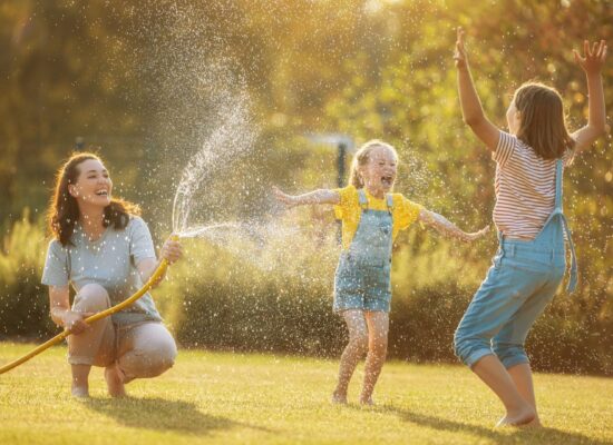 Family enjoying healthy backyard with children playing in water spray on lush green lawn
